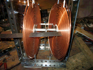 Close-up of two flat copper pancake coils mounted facing each other on a steel frame with a precise gap between them, nylon spacers and shims visible.