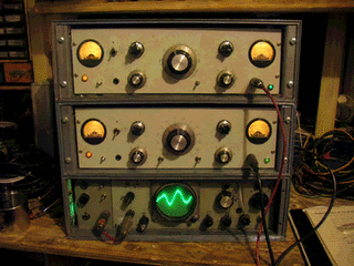 A rack of two vintage signal generators with large rotary knobs, illuminated dials, toggle switches and a small green oscilloscope showing a waveform.